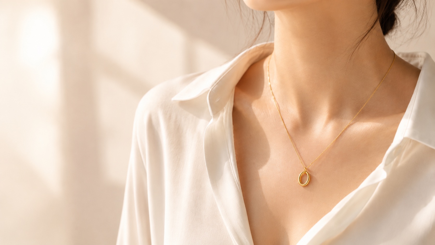 The Hollow Oval necklace worn close to the collarbone with a white shirt in warm light.